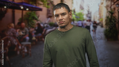 Фотография Man with frowning face standing in street cafe, arms at sides, looking at camera; subtle discontent