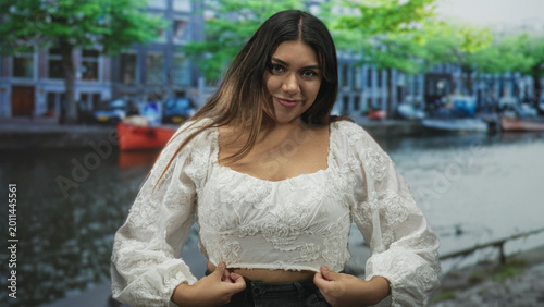 Bilde på lerret Woman adjusting blouse with hands on hem on street canal near boats and railing; confidence relaxed