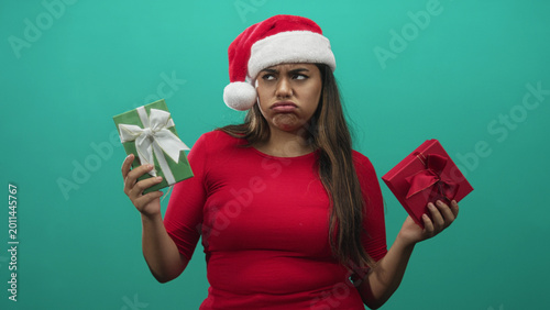 Quadro em tela Woman holding two wrapped gifts with pouting face wearing santa hat in studio; disappointment indecision