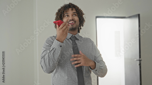Картината върху платно Man in shirt and tie holding red smartphone to mouth, gesturing with hand in building; confident sales pitch