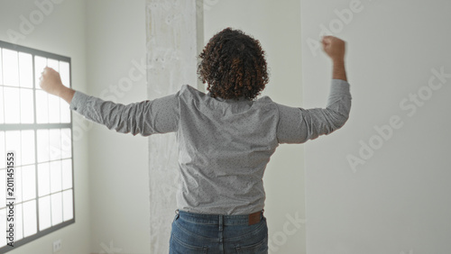 Valokuva Man raising arms toward window in empty building interior wearing shirt and jeans celebrating in an unfurnished house; new home joy