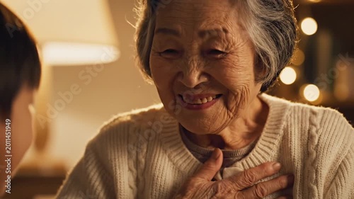 Happy Elderly Asian Woman in White Sweater Smiling Warmly While Interacting with Grandchild in Cozy Home Setting with Soft Lighting