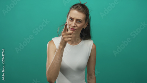 Bild auf Leinwand Woman, young caucasian in white sleeveless top pointing finger with raised hand in teal studio; disapproval
