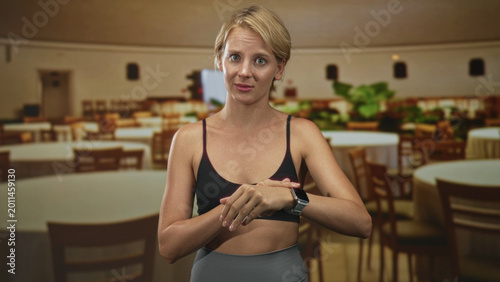 Foto Woman checking smartwatch and pointing at wrist amid a dining room with round tables and chairs in a building; impatience urgency