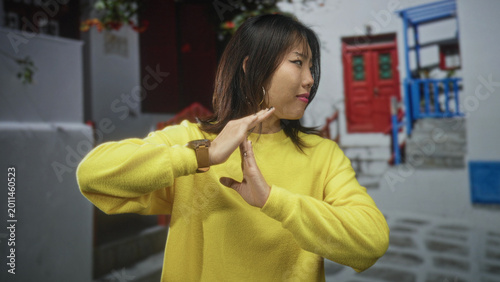 Bild auf Leinwand Woman in yellow sweater makes time out hand gesture with hands then crosses arms on cobbled street; personal boundary defiance