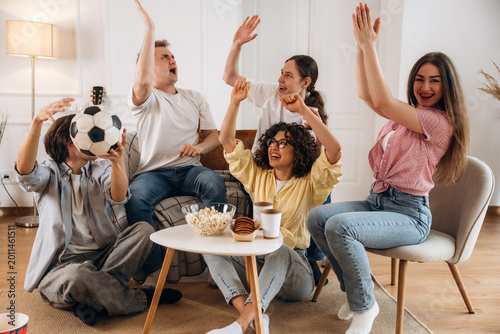 Foto Group of young adults celebrating and cheering while watching a soccer game at h