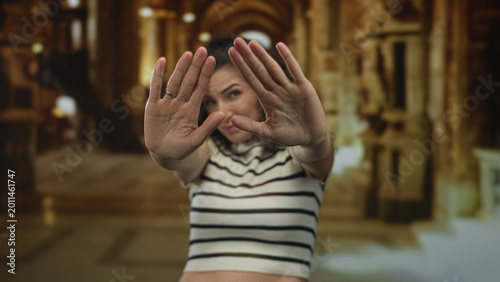 Photos Young hispanic woman blocks view with extended palms covering view partially in golden ornate building; rejection