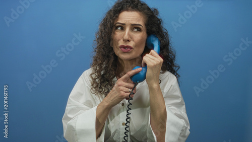 Foto Young hispanic woman holding retro telephone handset in blue studio; frustration urgency miscommunication