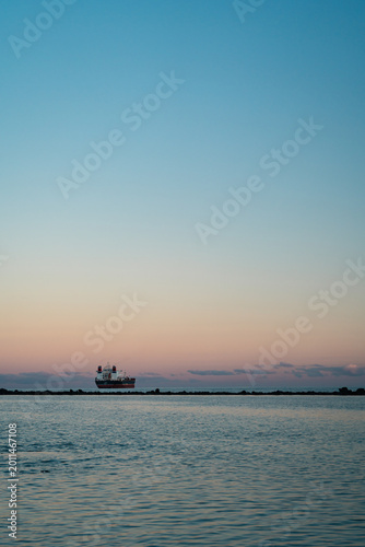 Cargo ship at dusk near breakwater with pastel sky