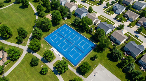 Aerial view of a blue pickleball court in a suburban neighborhood with green trees and houses