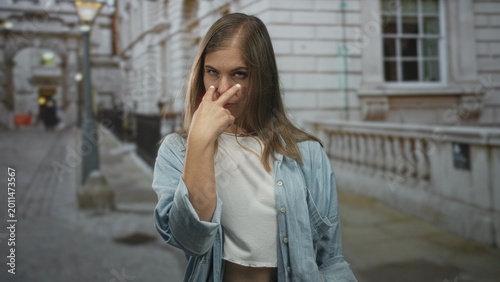 Schilderij op canvas Young blonde woman pointing finger with raised hand and serious expression on street by ornate building; confidence