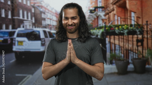 Quadro su tela Man with hands pressed together in prayer gesture on street in front of parked car and window boxes; gratitude serenity
