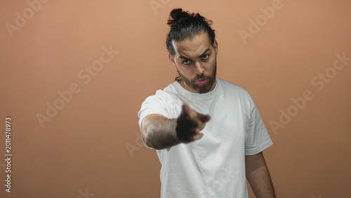 Bild auf Leinwand Man in white t shirt pointing finger at camera with stern expression in studio against peach wall; accusation anger