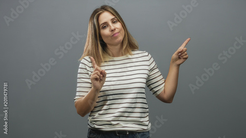 Obraz na płótnie Woman points index finger in studio wearing striped shirt and jeans with closed eyes and gray backdrop; indifference