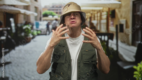 Fotografía Man with hands raised in a pleading gesture on a cobblestone street outside a cafe; desperation plea