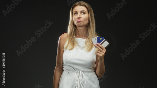 Valokuva Blonde woman holding creditcards in studio, right hand fanning three cards while looking skeptical and pursing lips; skepticism financial doubt