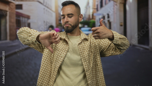 Bilde på lerret Man giving thumbs up and thumbs down on street with visible hands and thoughtful expression; ambivalence decision