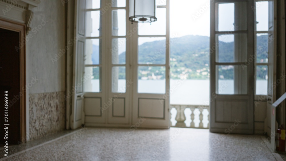 Fototapeta premium Interior room with open french doors leading to a lakeside balcony, soft defocused bokeh view of water and distant hills; background backdrop copyspace calm.