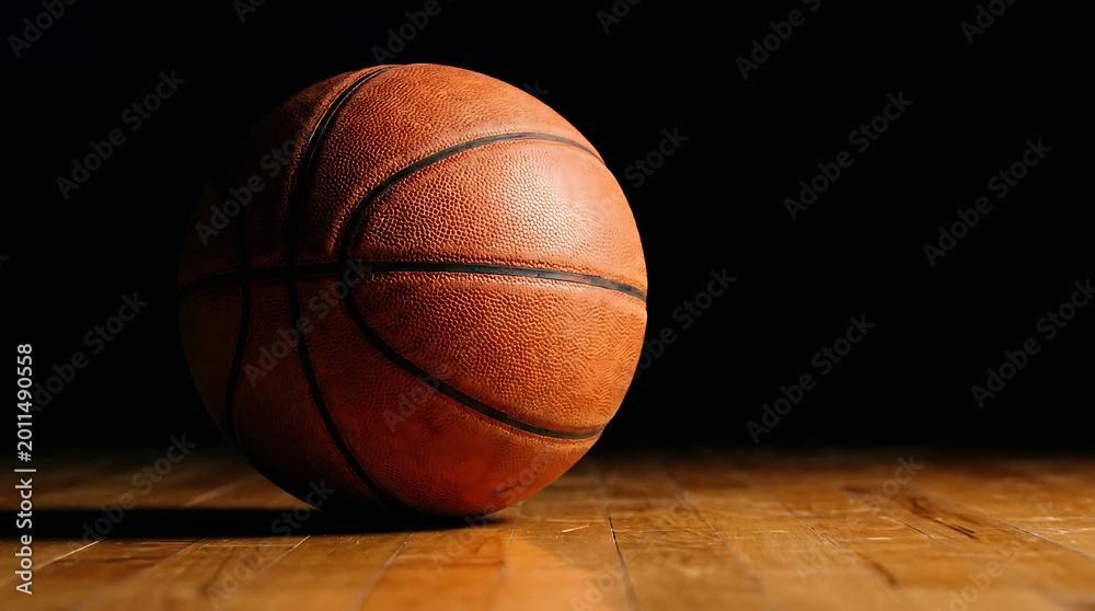 Obraz premium Orange basketball on hardwood court with dramatic lighting and dark background sports equipment