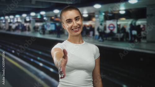 Quadro su tela Woman extends right hand for handshake on a subway platform at a station, short hair and white t shirt visible; welcome invitation