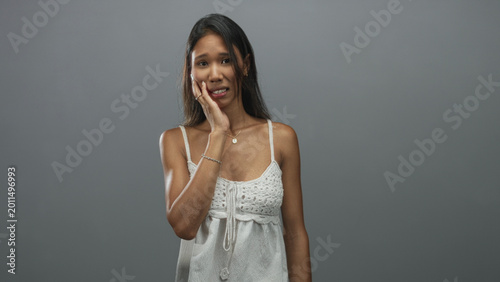 Εκτύπωση καμβά Thai woman pressing cheek with hand and grimacing, wearing white crochet camisole in a studio setting; toothache discomfort