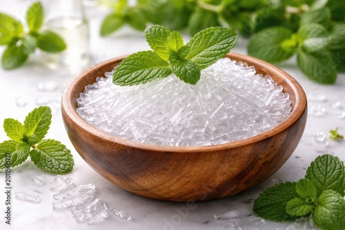 Natural wooden bowl holding menthol crystals topped by fresh peppermint on white
