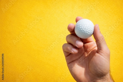 Yellow tee holding a golf ball with a simple bright yellow textured background and copy space