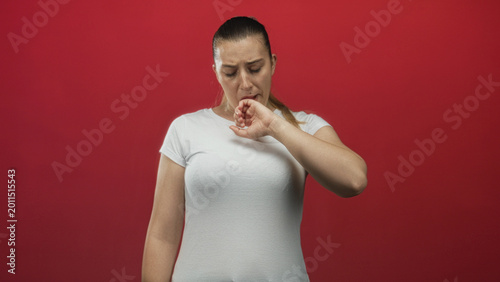 Bilde på lerret Woman gagging with hand to mouth, wearing white t shirt and ponytail against red studio wall; disgust nausea