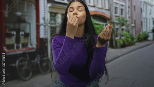 Cuadro en lienzo Woman wearing purple sweater pressing finger to lips gesture and raising other hand palm up on city street; serenity