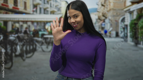Schilderij op canvas Young latin woman counts on fingers in a street scene with beige buildings and bicycles; playfulness