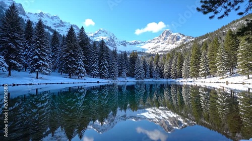 Snow-covered mountains and pine trees reflected in a calm lake during winter