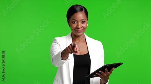African woman in business attire pointing at camera against green background