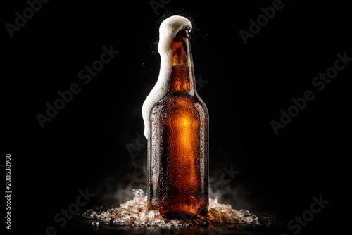 Foaming brown beer bottle highlighted on black background with copy space