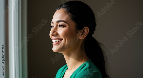 Young brunette woman smiling standing by the window in soft light. Positive emotions and well-being. Mental health concept. Diversity of appearances