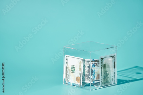US Dollar Bills Locked in a Transparent Glass Cube on Turquoise Background