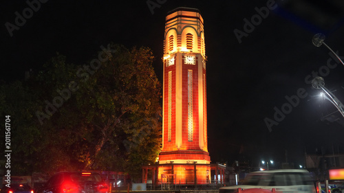 Night view of the illuminated Dehradun Clock Tower in Uttarakhand, India, glowing with warm architectural lighting against a dark sky. A landmark city scene featuring historic tower architecture