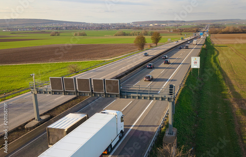 Aerial view of trucks and cars on the autobahn with the digital speed limit signs, traveling between agricultural fields 