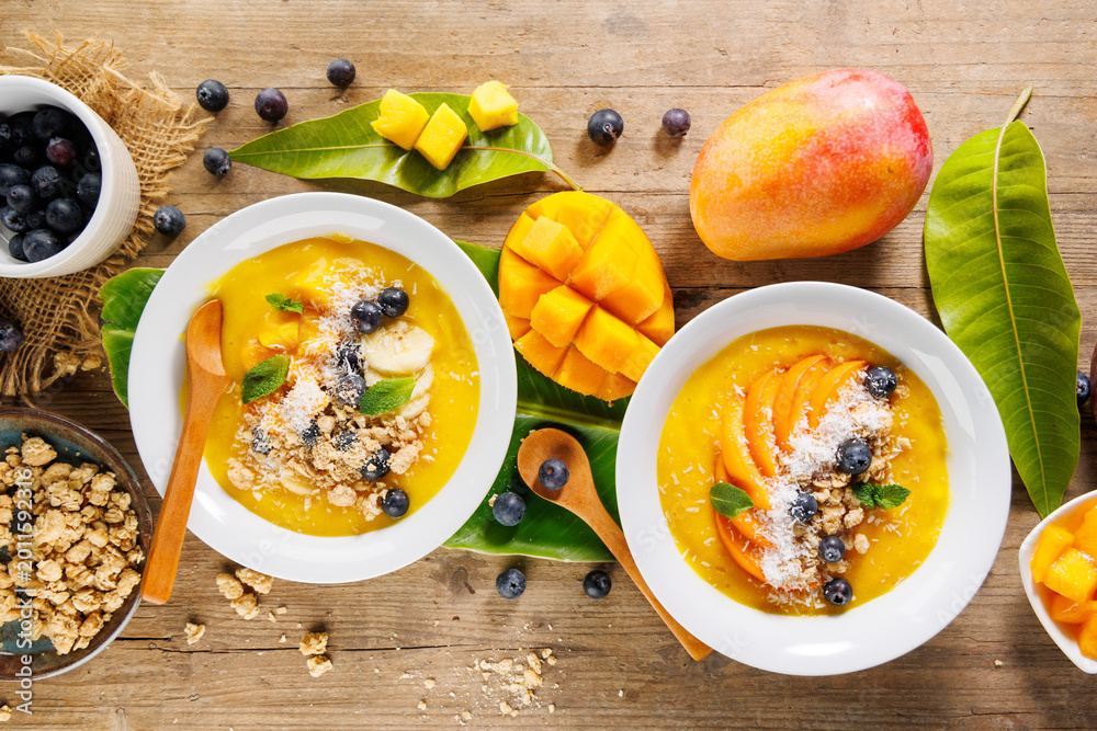Fototapeta premium mango smoothie bowls with granola and blueberries for healthy breakfast