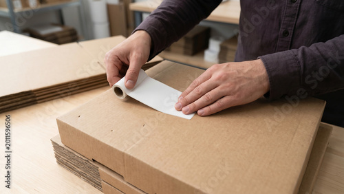 Hands applying label sticker to box surface, flat angle, clean commercial stock photography, 8k high resolution quality.
