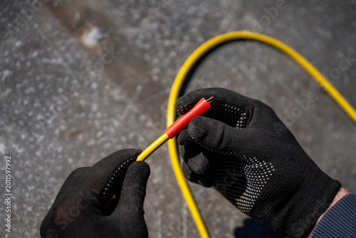 Konstfotografi Gloved hands placing a red heat shrink tube over a yellow electrical cable beside a kit of colored shrink tubing outdoors