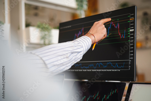 A person's hand points to a financial chart on a computer screen, analyzing market data.