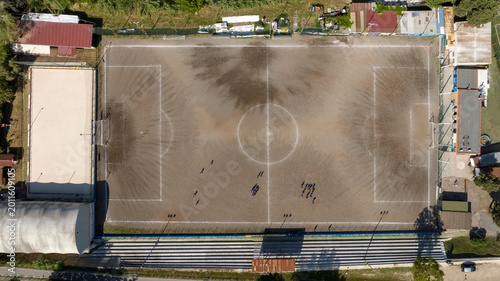 Photos Top-down aerial view of a dirt soccer field featuring players, white boundary lines, and a central circle