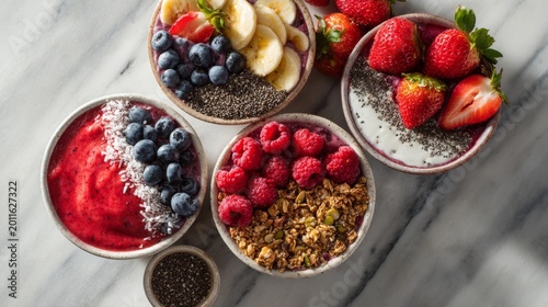 Close-up of four colorful smoothie bowls, laden with fresh fruits, granola, and chia seeds, atop a marble surface