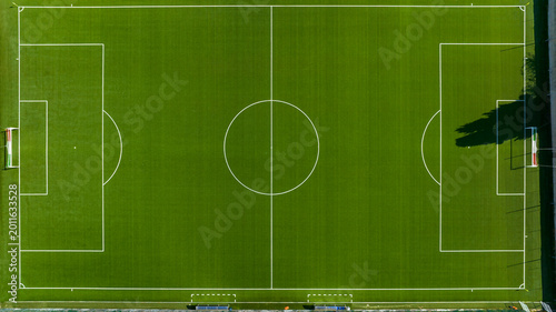 Fotografía Perpendicular top-down aerial view of a vibrant green synthetic soccer field, showcasing precise white boundary lines, the center circle, penalty areas, and goals under clear, bright daylight
