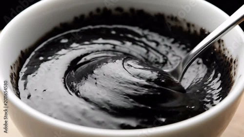 Close up of black viscous liquid being stirred in a white bowl, smooth texture, macro shot
