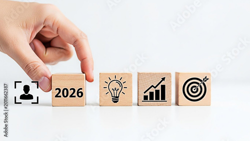 Hand placing wooden blocks with business icons representing growth strategy for the upcoming year 2026