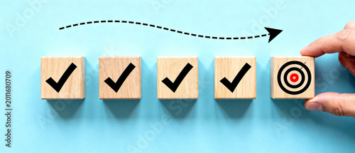 Achieving business goals by completing tasks in a strategic and organized manner, represented by wooden blocks with checkmarks and a bullseye