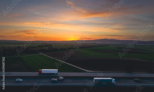Semi trucks and cars traveling on the highway at sunset with colorful sky and countryside view