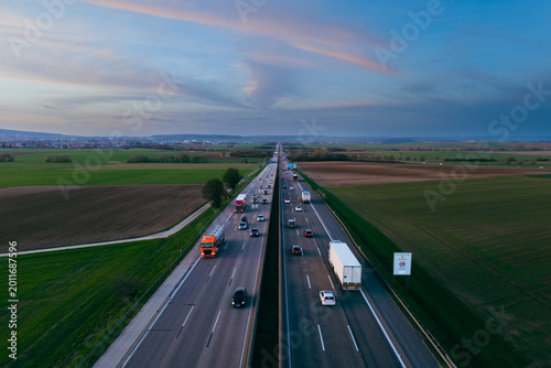 Aerial view of a highway with various vehicles between farmland in the evening.
