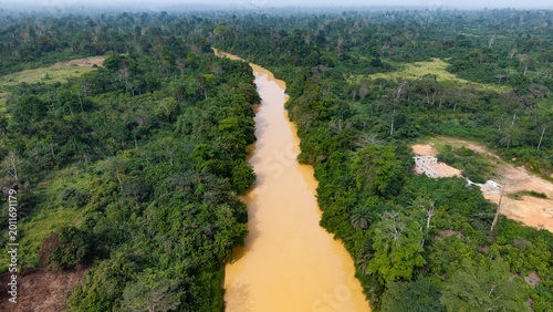Slika na platnu Brown, muddy river flowing through a deforested landscape, showing environmental